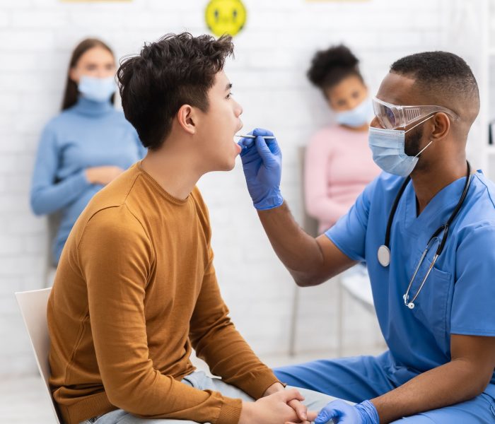 African Doctor Testing Asian Patient For Coronavirus Sitting In Clinic